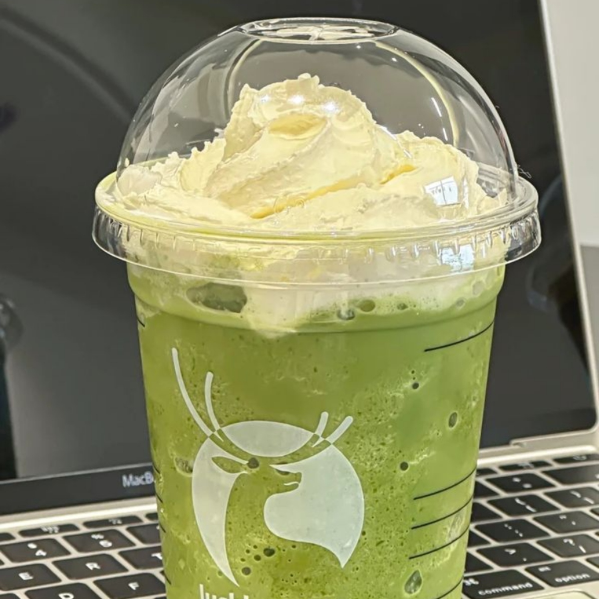 Green matcha smoothie with whipped cream in a plastic cup on a laptop keyboard