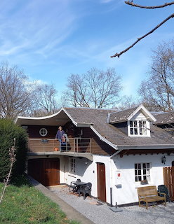 Two-story white house with dark brown roof, garage, and dormer window, framed by leafless trees
