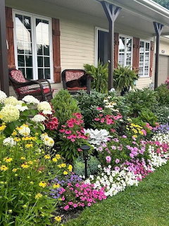 Colorful flower garden with hydrangeas and mixed bloms in front of a house porch with wicker chairs