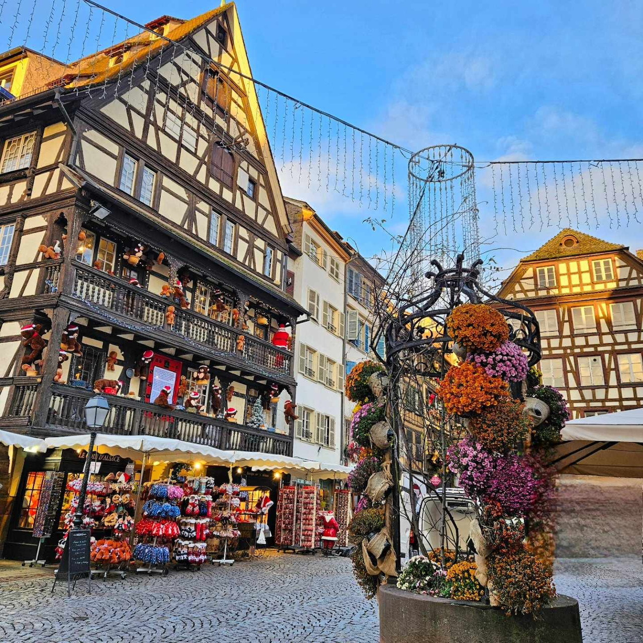Christmas market square in Strasbourg with half-timbered buildings, decorated fountain, and holiday lights at dusk