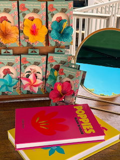 Colorful tropical flower paintings and notebooks displayed on wooden table with white furniture