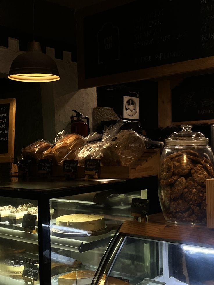 Dark cozy café interior with bakery display counter, glass cookie jars, bagged pastries, and hanging pendant lamp