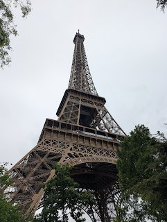Eiffel Tower seen from ground level looking up against an overcast sky with green trees at the base