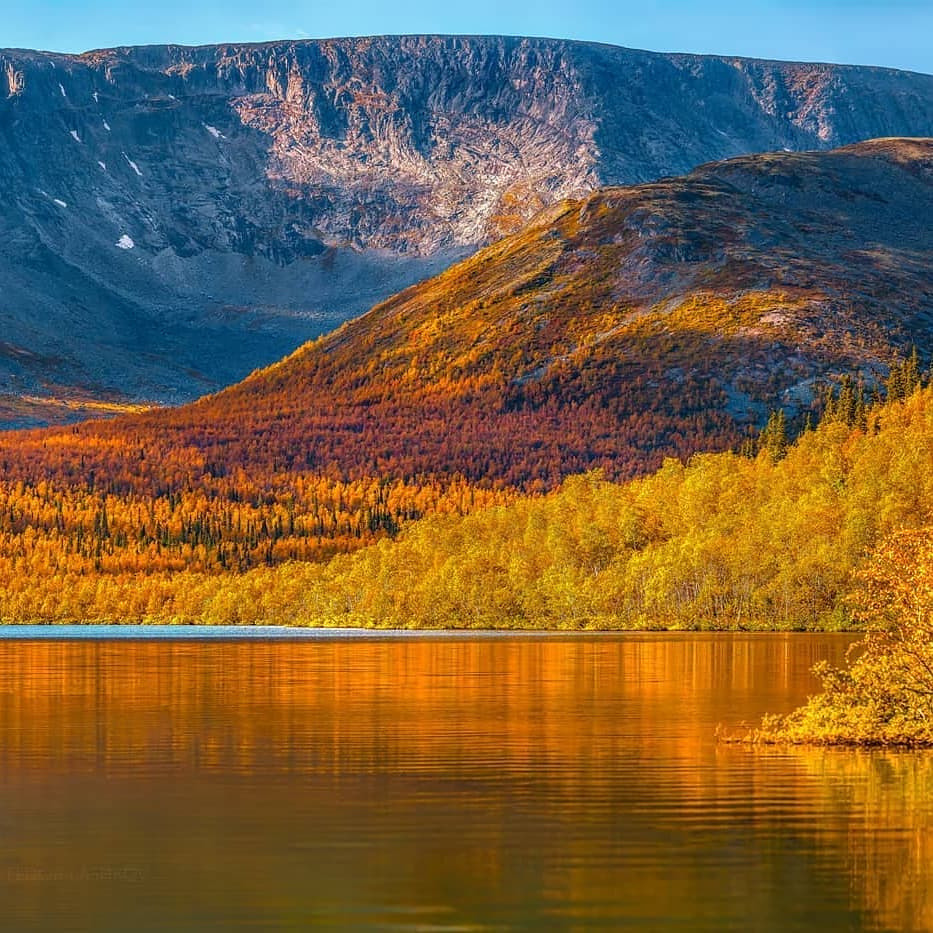 Mountain lake with autumn forest and rocky plateau reflected in calm water
