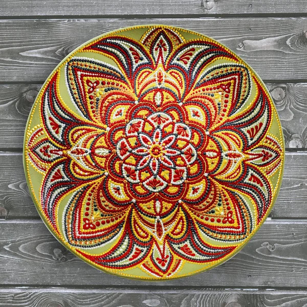 Decorative plate with intricate mandala pattern in warm orange and red tones on wooden surface