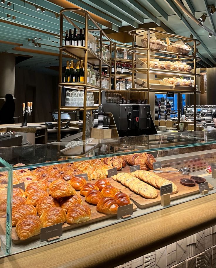 Glass bakery display case with croissants and pastries, shelves of bread visible in background
