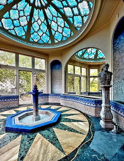 Art deco interior with turquoise stained glass dome ceiling, mosaic floor, and fountain in sunlit room with arched windows