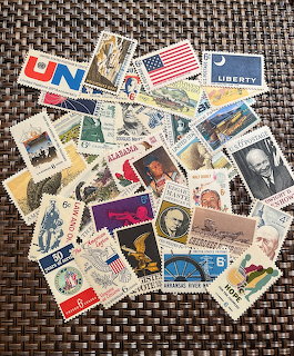Pile of assorted vintage US postage stamps scattered on a brown woven mat