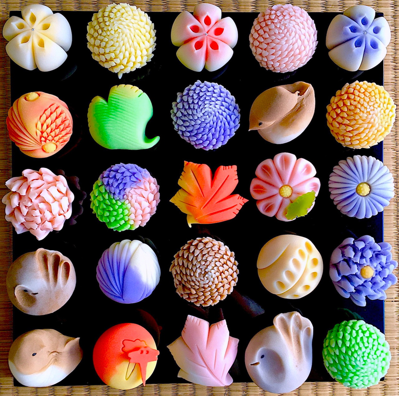 Grid of colorful Japanese wagashi sweets with flower and geometric patterns on black background