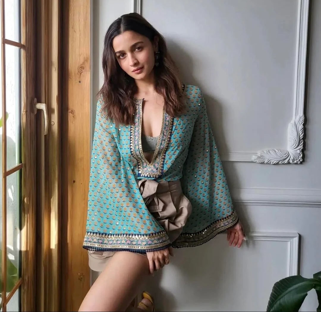 Young woman in turquoise printed outfit posing against a white wall indoors