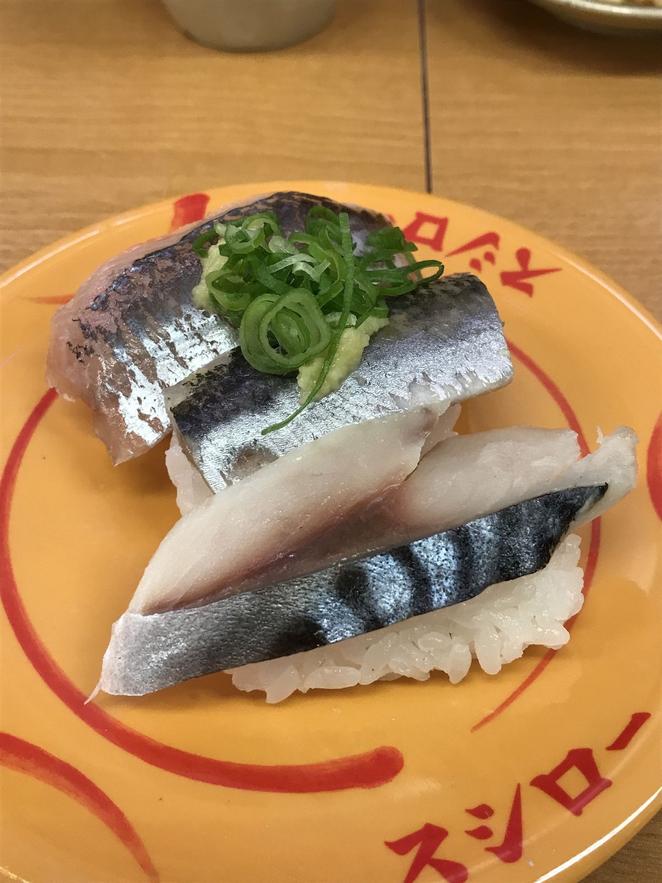 Two pieces of mackerel nigiri sushi garnished with sliced green onion on a yellow plate