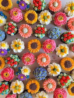 Assortment of cupcakes topped with colorful buttercream flowers including sunflowers, roses, and daisies