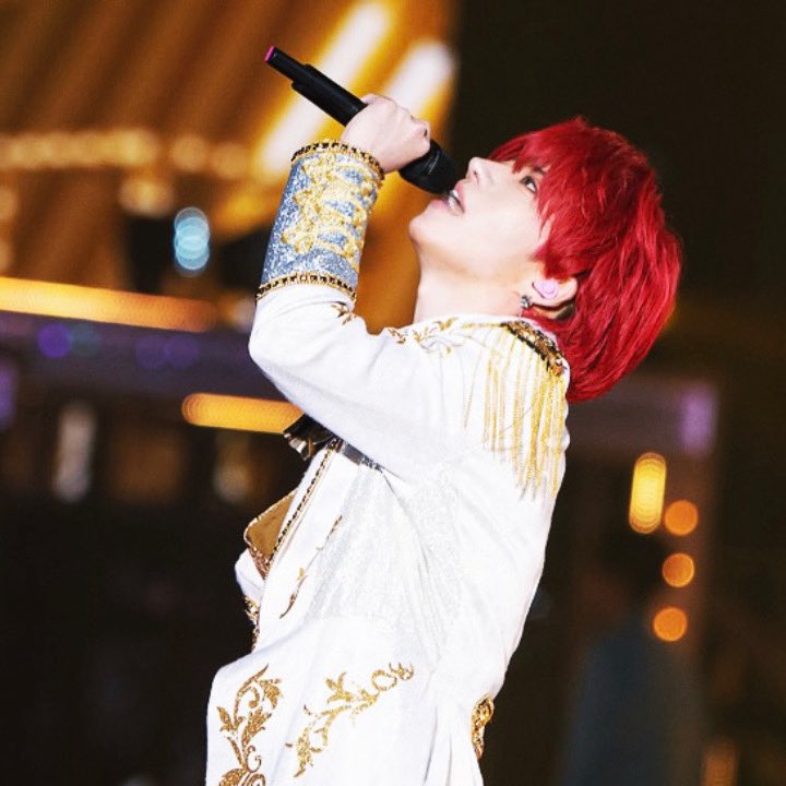 Red-haired singer in a white embroidered jacket singing into a microphone on stage