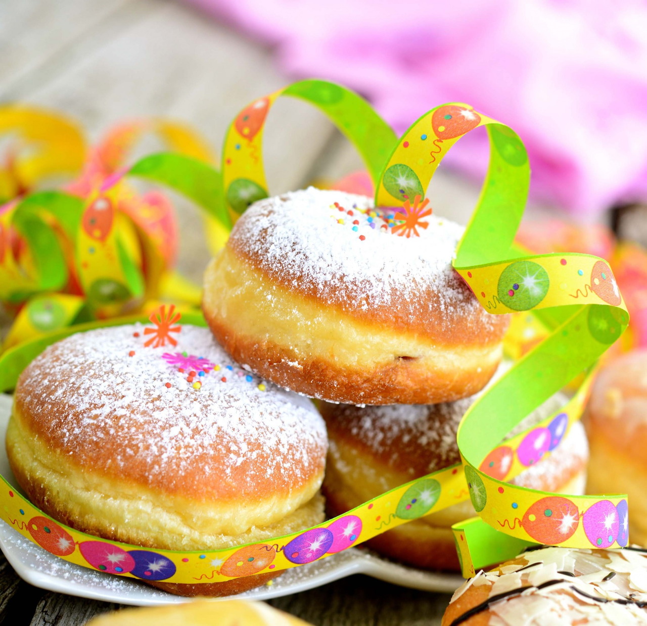 Two powdered sugar jelly doughnuts surrounded by colorful curled ribbons