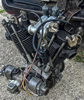 Vintage JAP v-twin motorcycle engine with black cylinder fins, wiring, and dynamo on pavement