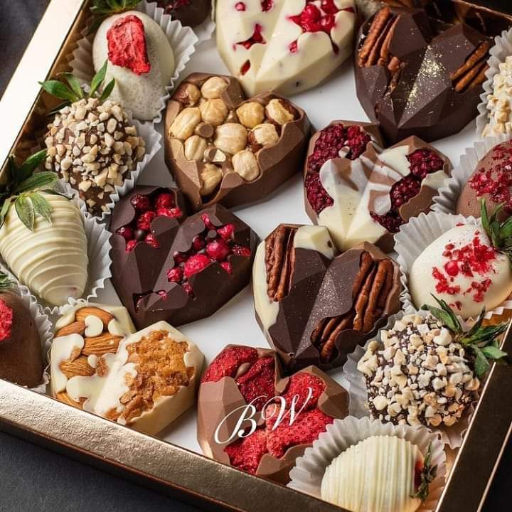 Box of decorated heart-shaped chocolates with various toppings including nuts, berries, and white chocolate drizzle
