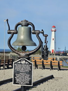 Bronze bell monument with plaque and a white lighthouse in the background