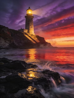 Glowing lighthouse on rocky shore at sunset above the sea