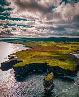 Green coastal cliffs and a sea stack at Downpatrick Head under dramatic clouds