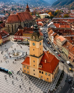 Aerial view of a historic Romanian town square with a clock tower, church, and red rooftops