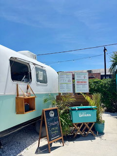 Turquoise Airstream trailer café with chalkboard menu and folding chairs on sunny day