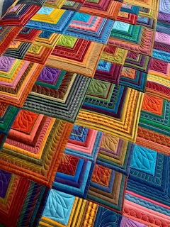 Colorful patchwork quilt with geometric concentric squares in vibrant red, blue, yellow, and green fabrics