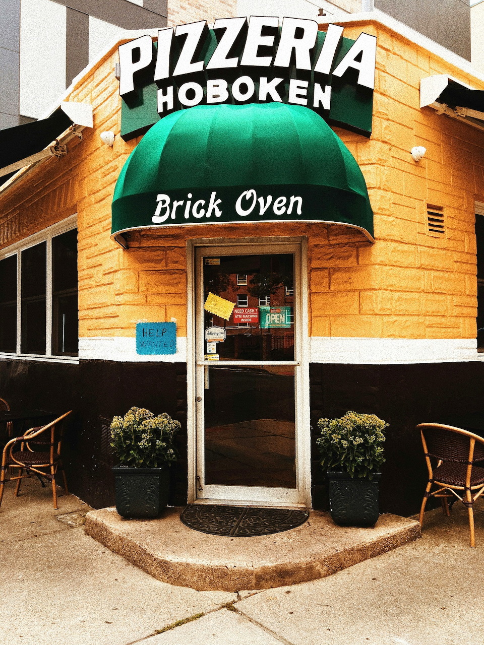 Corner entrance of yellow pizzeria building with green awning and brick oven sign