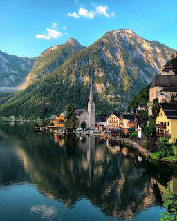 Lakeside village with church steeple, mountain backdrop, and reflections in calm water