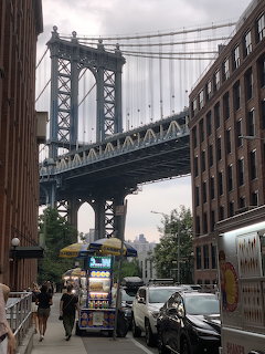 Manhattan Bridge seen from DUMBO Brooklyn street with brick buildings, cars, and a food vendor cart