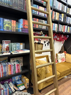Wooden ladder leaning against dark bookshelves with a yellow cushioned reading nook below