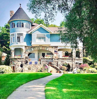 Victorian mansion with blue turret and stone foundation on green lawn