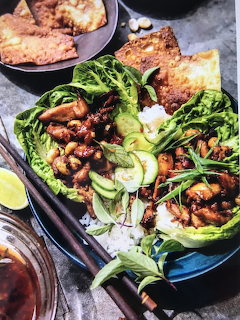 Overhead view of Thai dishes: fried chicken, stir-fried greens, and shrimp lettuce wraps on dark plates