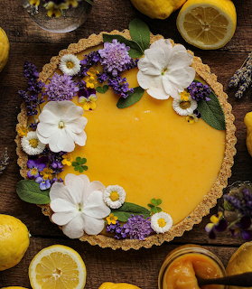 Overhead lemon tart with white flowers, lavender, and lemon halves on a wooden table