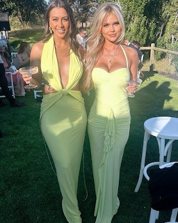 Two women in low-cut green dresses posing together at an outdoor garden event