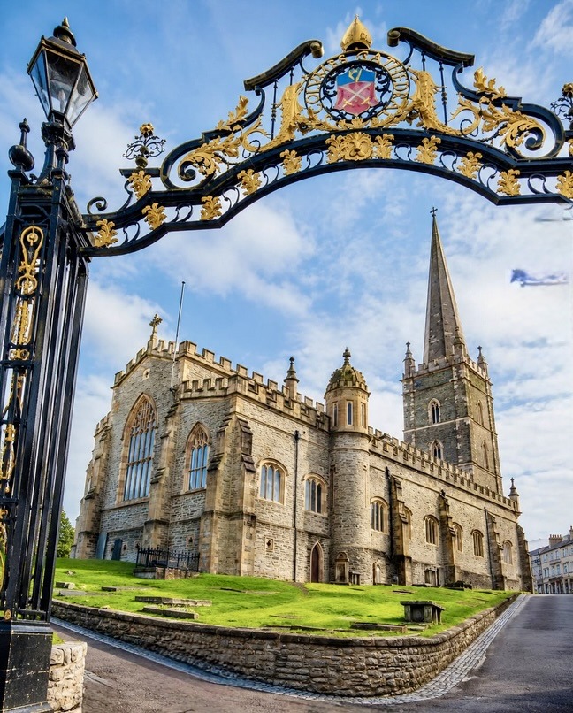 Stone cathedral with tall spire viewed through ornamental iron gates on a sunny day