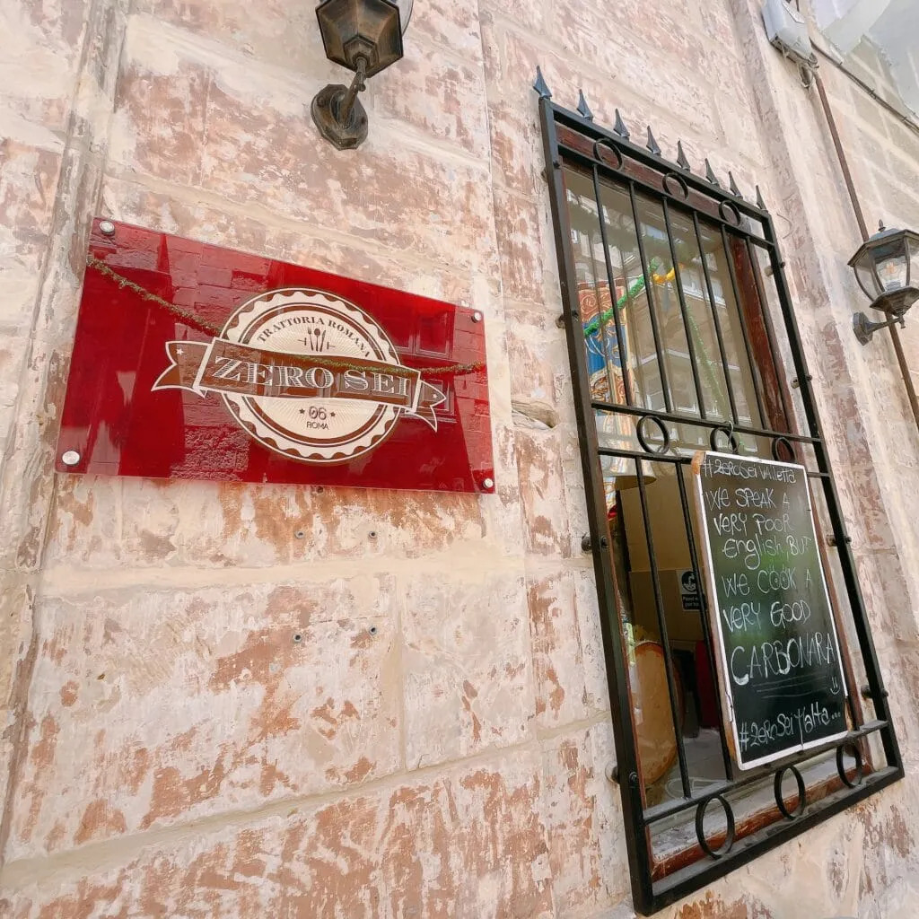 Limestone building wall with red sign reading Zero Sei and window with iron bars and chalkboard menu