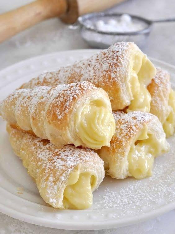 Custard-filled Italian puff pastry cones dusted with powdered sugar on a white plate.