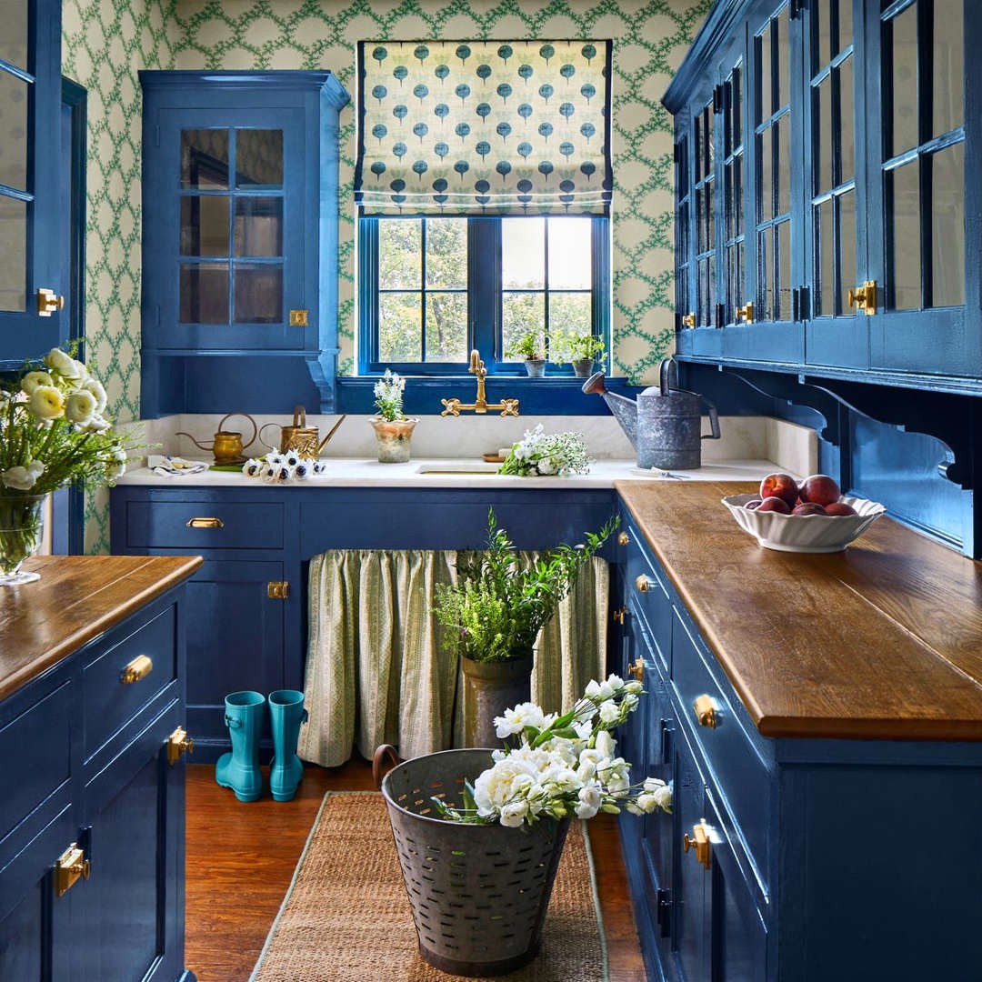 Cobalt blue kitchen with wooden counters, patterned wallpaper, window, and flowers in metal bucket