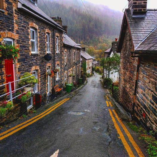 Steep village street with stone houses and misty hills