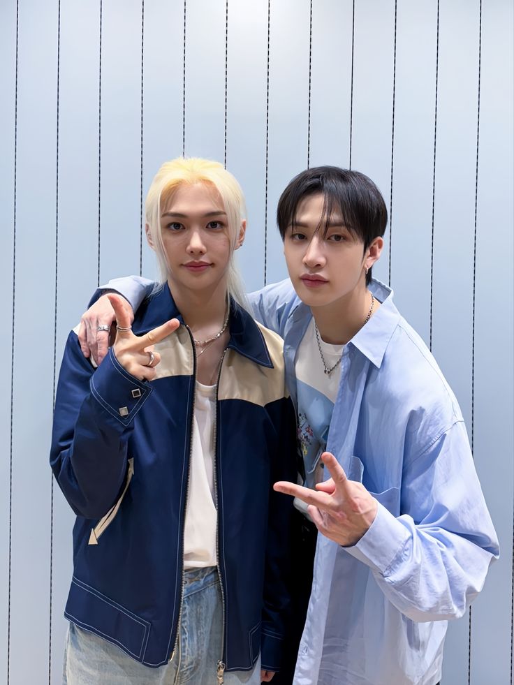 Two young men posing with peace signs, one blonde in blue jacket, one dark-haired in blue shirt