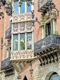 Ornate historic building facade with detailed stone carvings, bay windows, and wrought iron balconies in Barcelona