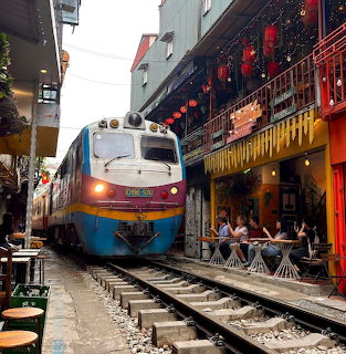 Passenger train moving through narrow street between traditional buildings with red lanterns and outdoor seating