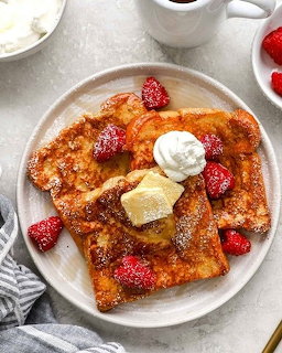French toast with butter, whipped cream, and strawberries on white plate