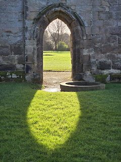 Sunlight shining through a medieval Gothic stone archway in castle ruins onto green grass