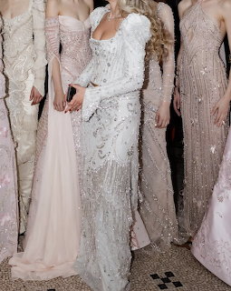 Women in sequined and beaded white and blush evening gowns standing together backstage