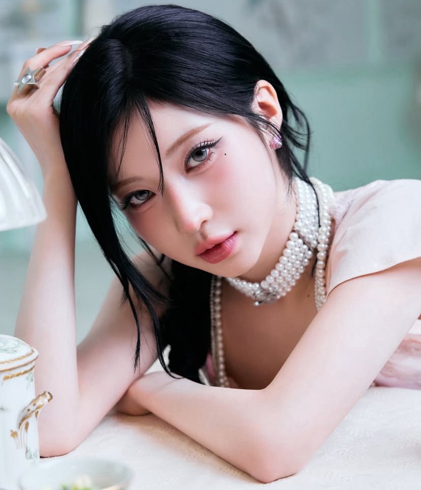 Young woman with black hair wearing pearl necklace posing with hand in hair in soft indoor light