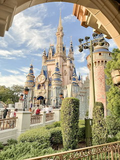 Cinderella Castle at Disney World Magic Kingdom viewed through an archway with blue sky and topiaries