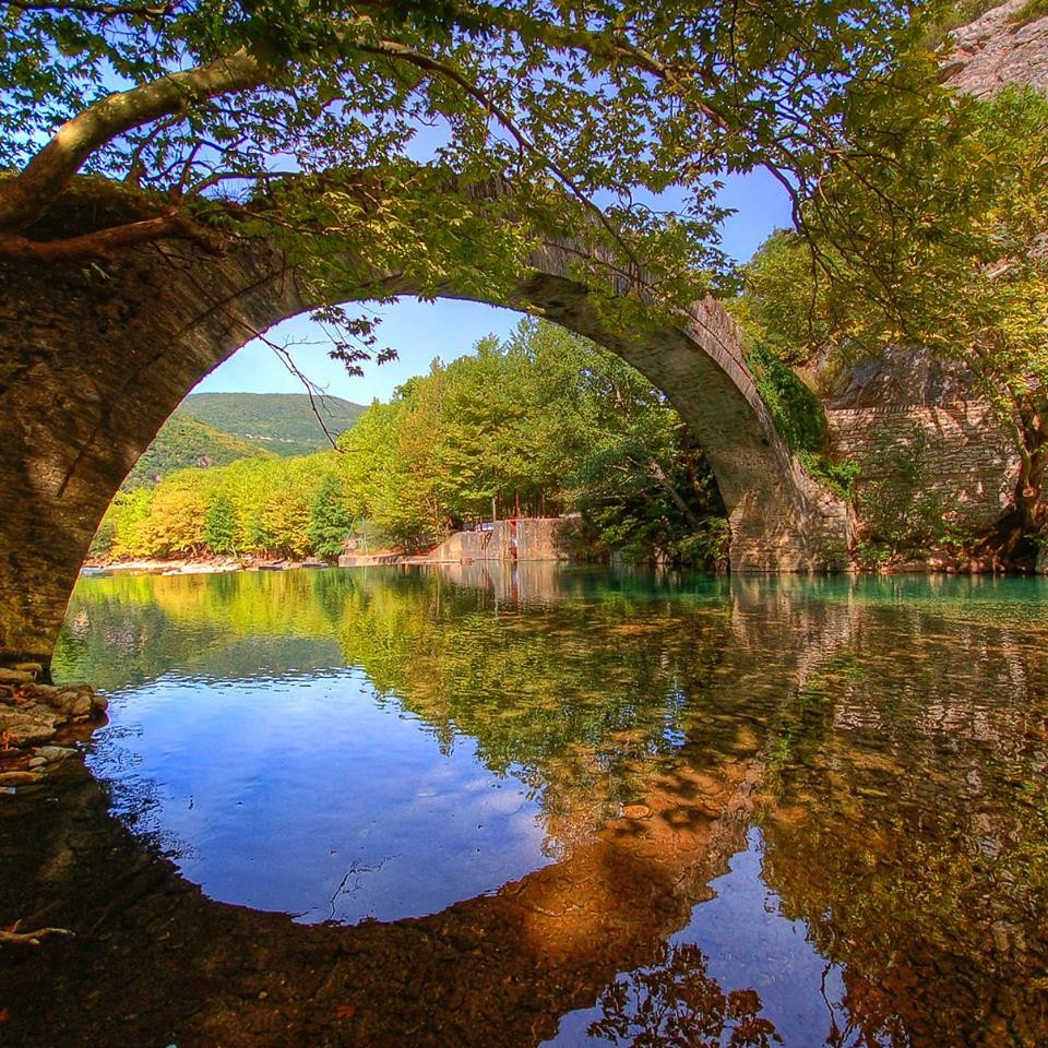 Stone arch bridge over still lake with mirror reflection and green foliage