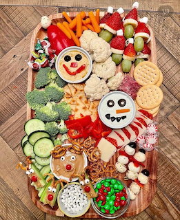 Christmas-themed snack board with vegetables, fruits, crackers, dips decorated as snowman and reindeer faces, and holiday candy