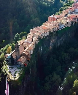 A narrow village perched on a tall basalt cliff above a forested valley